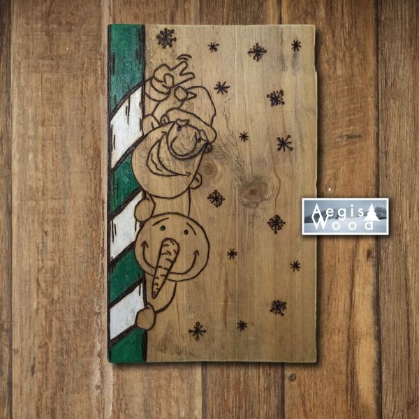 Tableau de Noël vert et blanc pyrogravé sur bois : bonhomme de neige et Père Noël derrière un sucre d'orge, flocons de neige tout autour